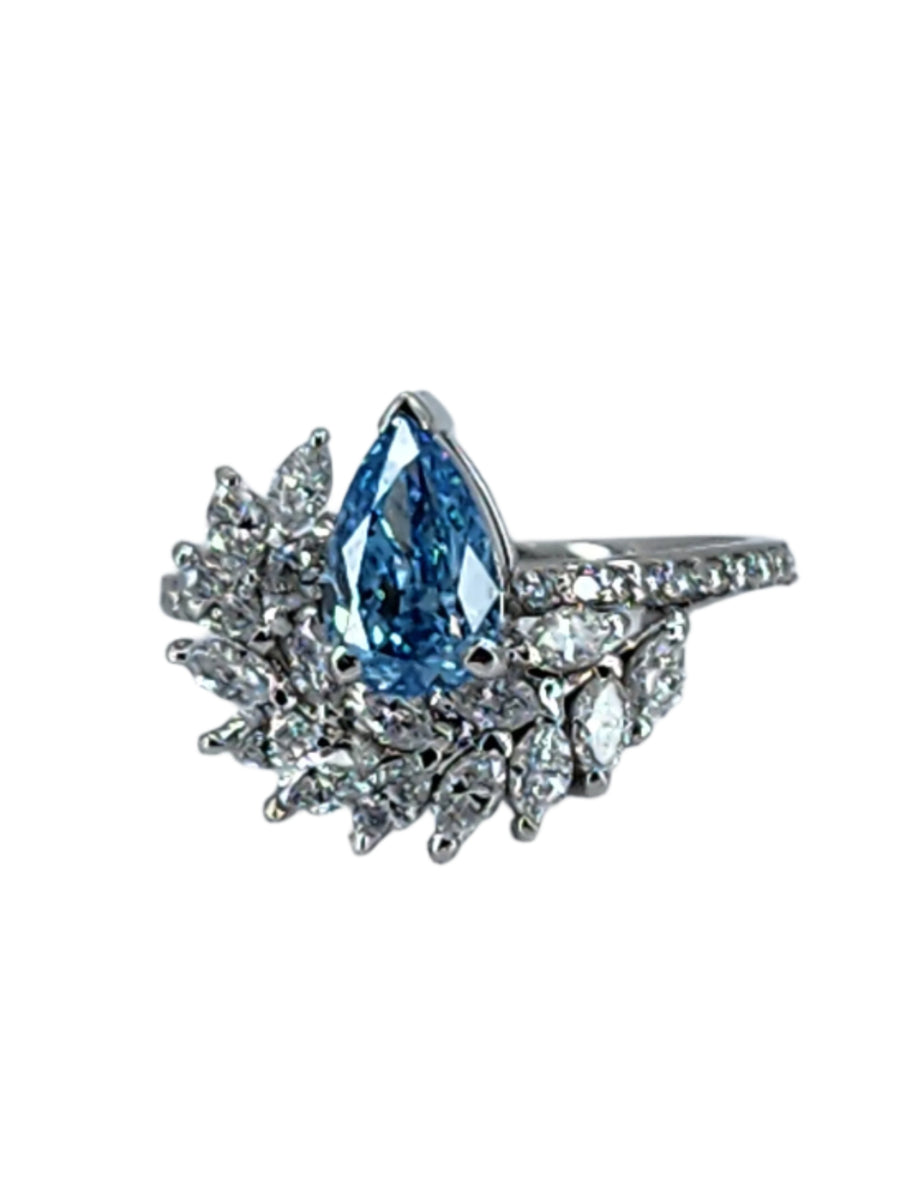 Close-up view of a blue lab grown pear cut diamond ring with a 1-carat centerpiece and white marquise cut cluster, emphasizing the intricate details and sparkling facets of the 1.85 TCW design.

