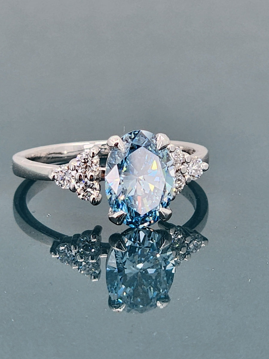 Angled perspective of a blue lab-grown oval cut diamond ring, emphasizing the depth and brilliance of the 1.95-carat center stone.

