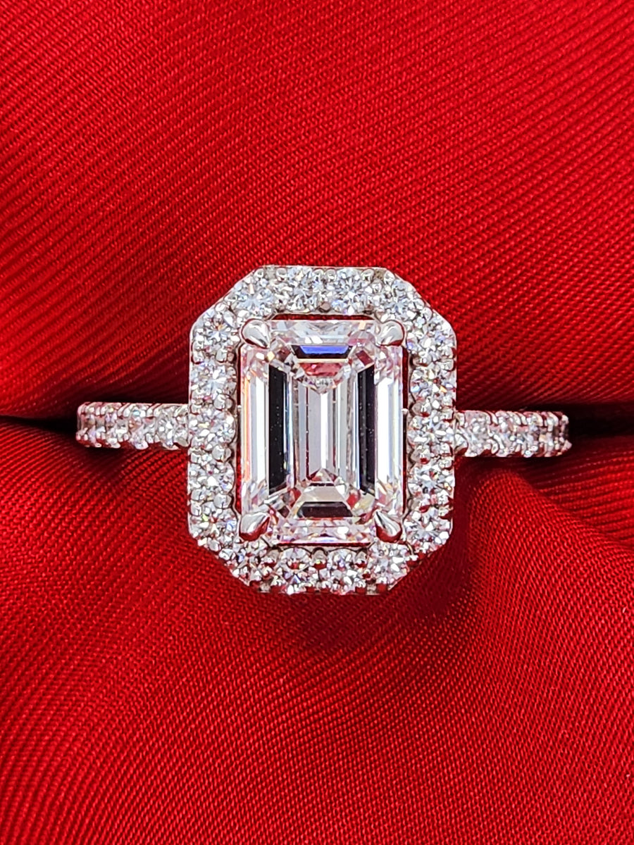 Lab grown emerald cut diamond ring with halo design displayed against a bold red fabric, showcasing brilliance and sparkle in a 2.31 carat center stone.